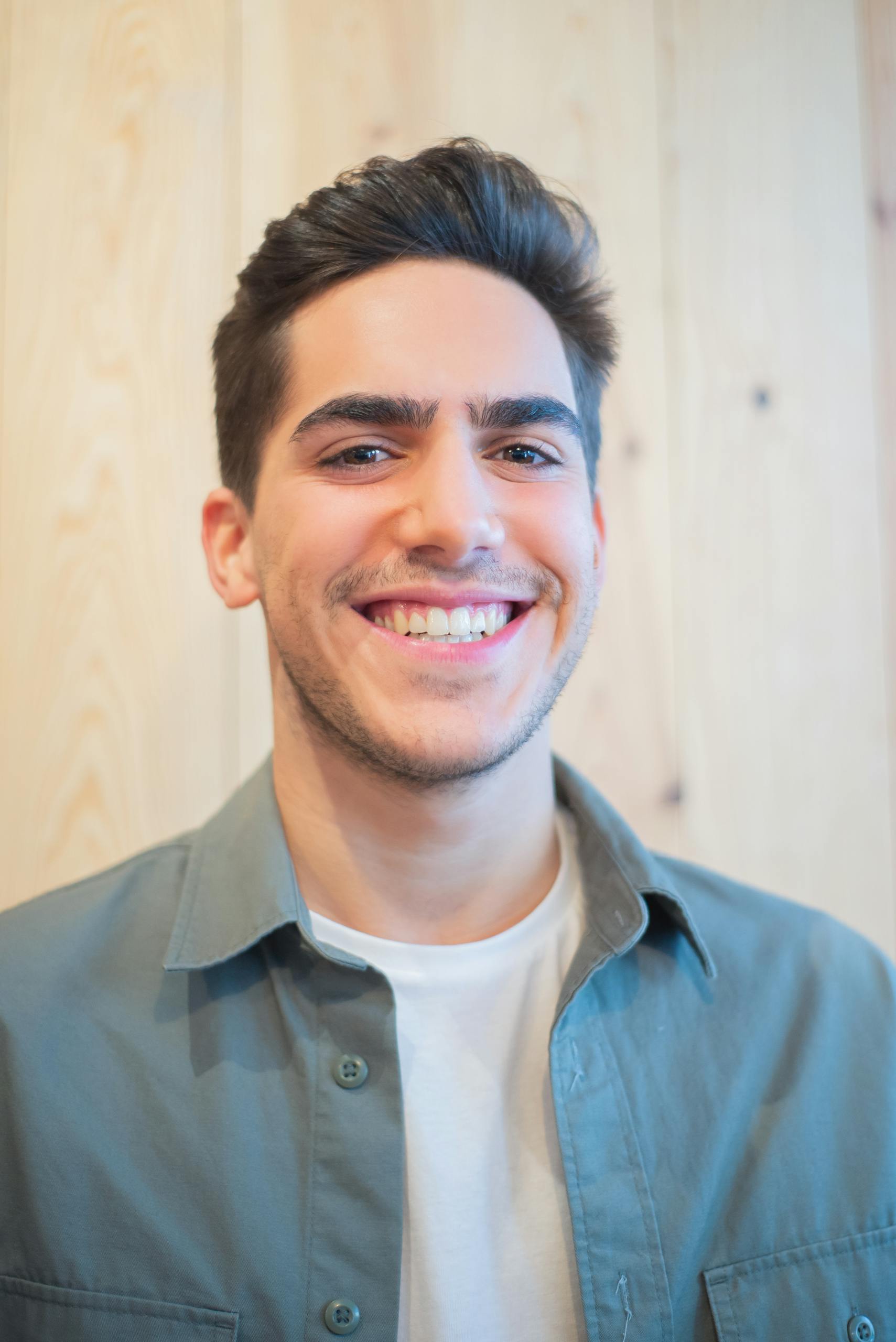 Happy young man smiling indoors, wearing a white shirt and casual jacket.
